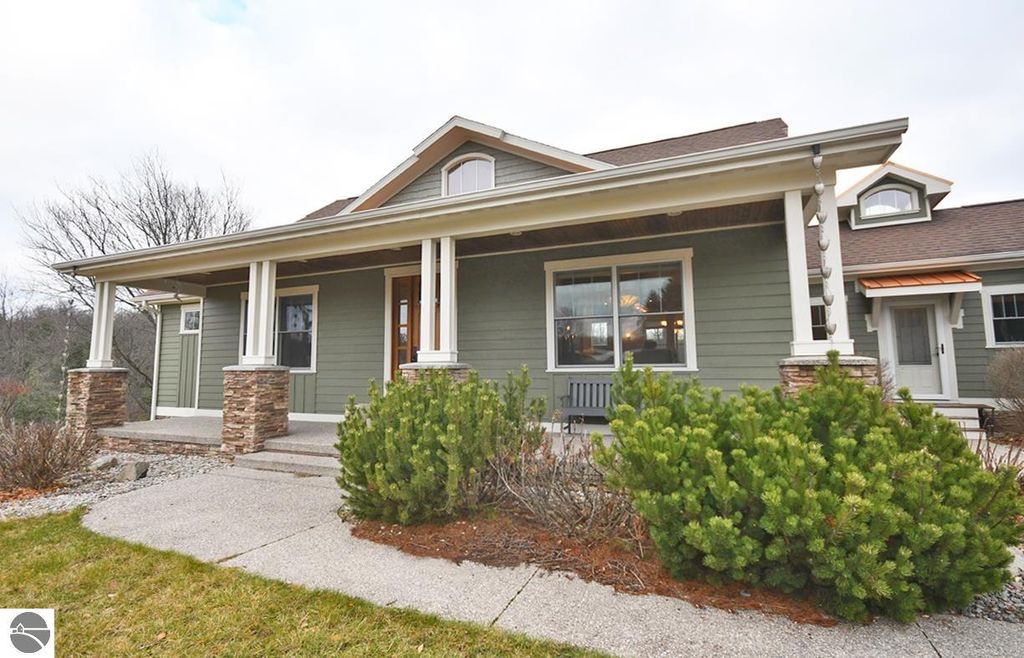 Stately four-bedroom home exterior at 11007 S Rolling Meadows Drive, featuring a welcoming porch, stone accents, and landscaped yard in Maple City, MI.