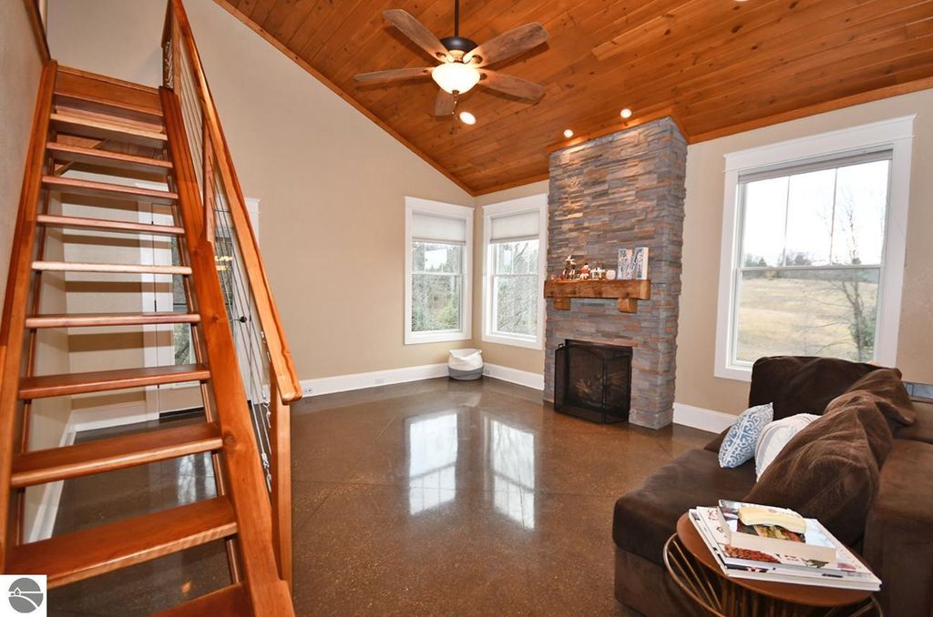 Cozy living room featuring vaulted wood ceiling, stone fireplace, and wooden staircase, showcasing the open floor plan of the Maple City home at 11007 S Rolling Meadows Drive.