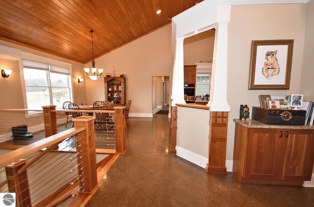 Interior view of a spacious home featuring a vaulted wood ceiling, dining area with wooden chairs, decorative shelving, and polished concrete flooring, emphasizing the craftsmanship and open layout of the property at 11007 S Rolling Meadows Drive, Maple City, MI.