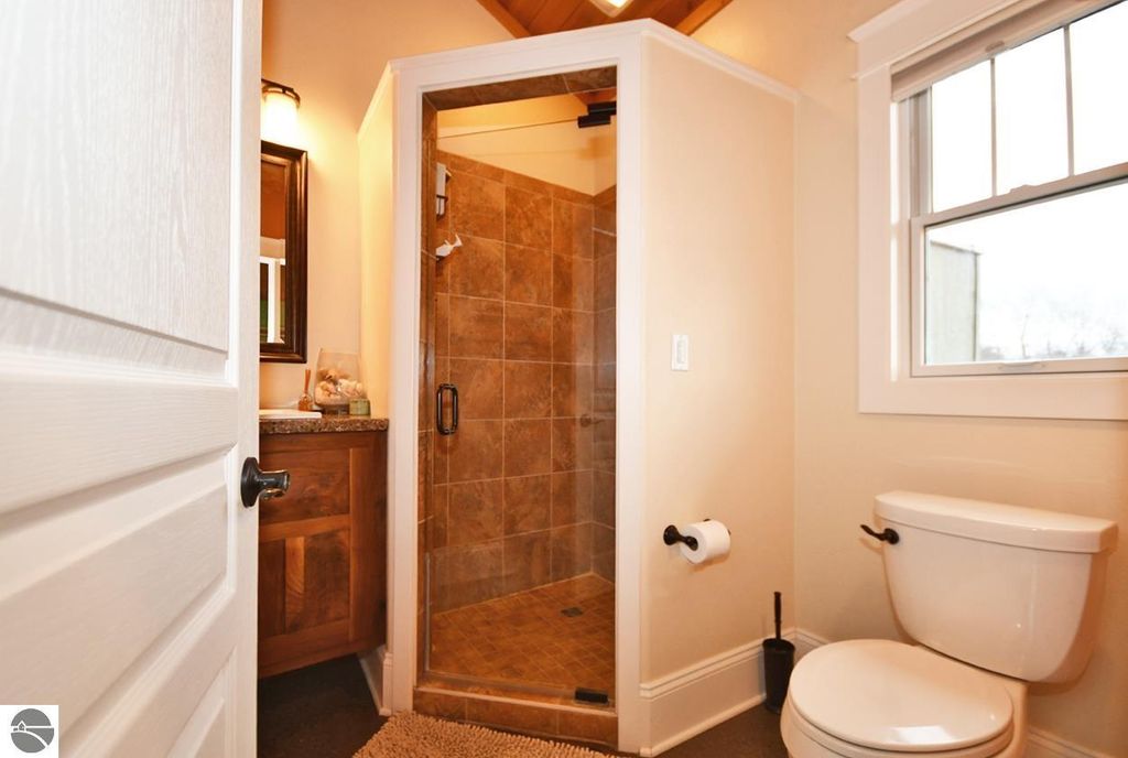 Modern bathroom featuring a walk-in shower with tiled walls, wooden cabinetry, and a window, showcasing elegant design elements suitable for a home listing in Maple City, MI.