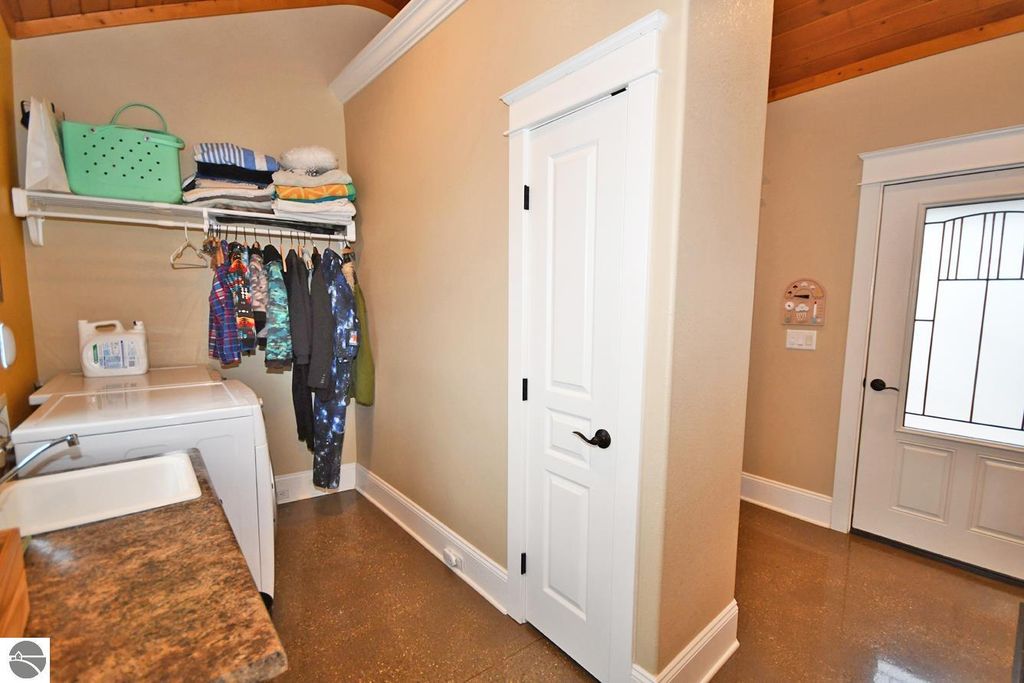 Laundry room with washer, organized shelves, hanging clothes, and a door leading outside, showcasing the practical features of the home at 11007 S Rolling Meadows Drive, Maple City, MI.