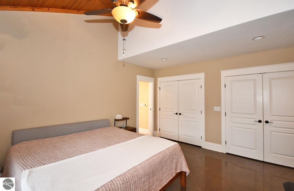 Spacious bedroom featuring a large bed, vaulted ceiling, and double doors leading to a closet, showcasing modern design elements in a Maple City home for sale.