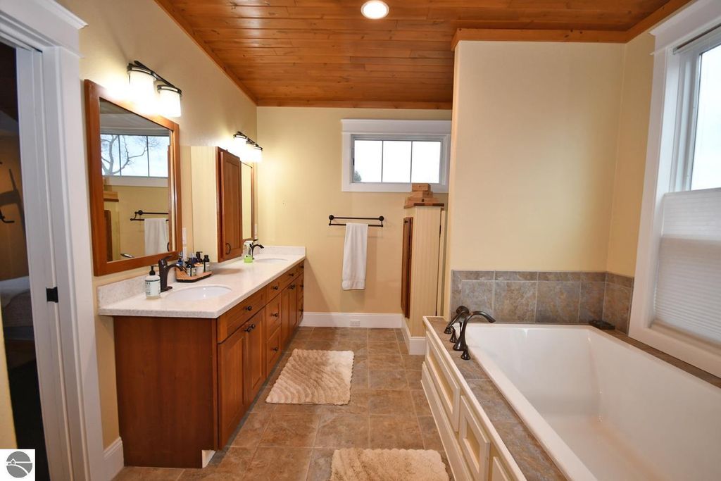 Spacious bathroom featuring dual vanities with wooden cabinetry, a soaking tub, and natural light from windows, showcasing a blend of modern design and rustic charm in a Maple City home.