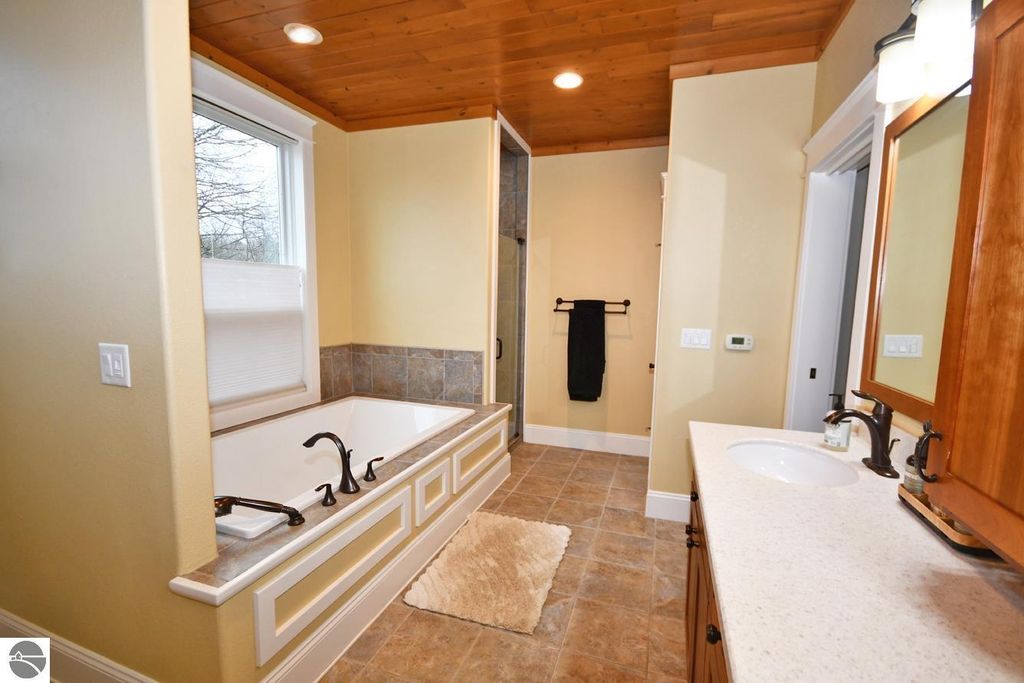 Spacious bathroom featuring a soaking tub, dual sinks, natural wood ceiling, and a tiled shower area, showcasing modern design elements and ample natural light.