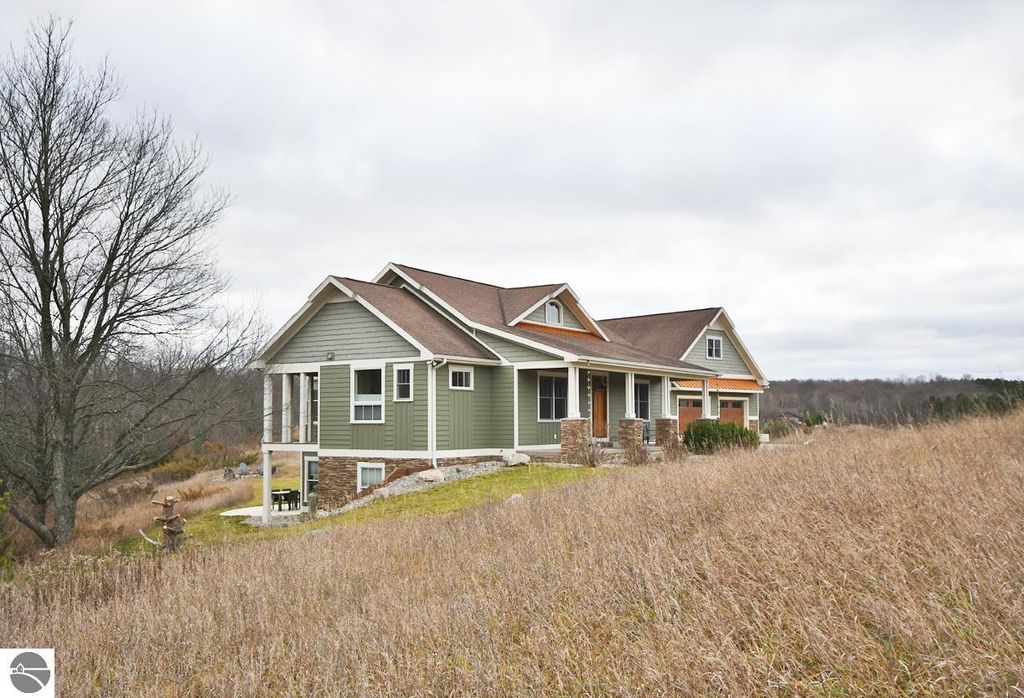 Stately four-bedroom home on 9.9 acres in Maple City, MI, featuring a modern design with a green exterior, multiple gables, and scenic hillside surroundings.
