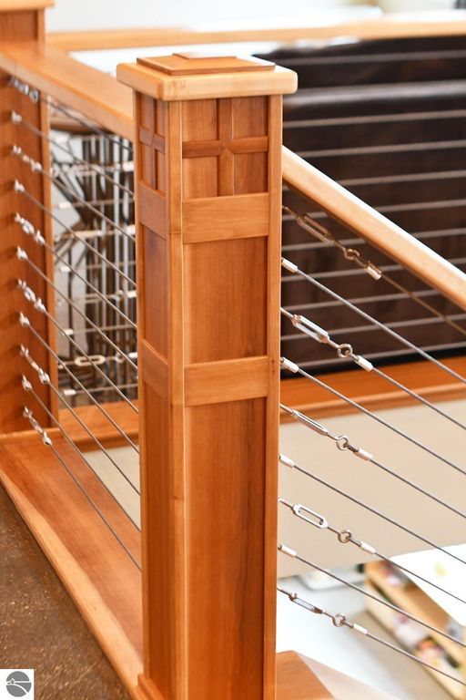 Close-up of a wooden railing post with intricate craftsmanship and metal cable detailing, showcasing the modern design elements of the interior of a luxury home at 11007 S Rolling Meadows Drive, Maple City, MI.