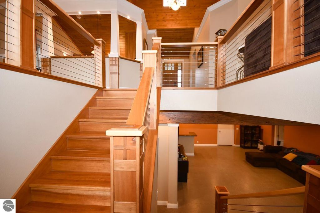 Interior view of the staircase in a modern home featuring wooden steps, railing with metal wire accents, vaulted ceilings, and an open floor plan leading to a spacious living area, showcasing the craftsmanship and design of the property at 11007 S Rolling Meadows Drive, Maple City, MI.
