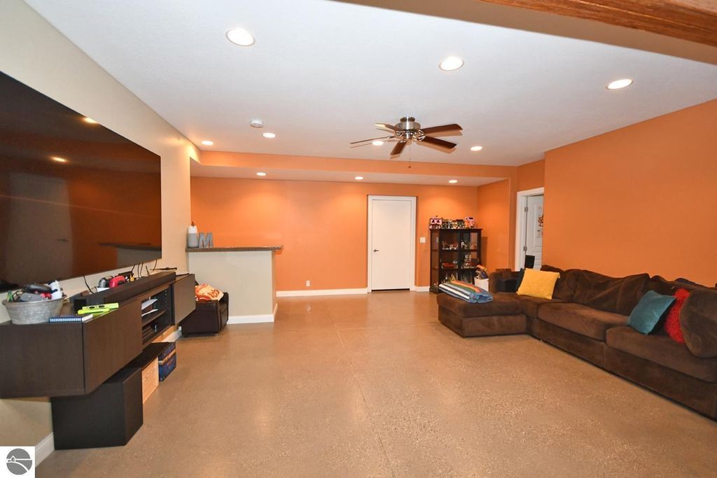Spacious walkout lower level living area featuring a large sectional couch, entertainment unit, and an open layout with warm orange walls, ideal for relaxation and entertaining.
