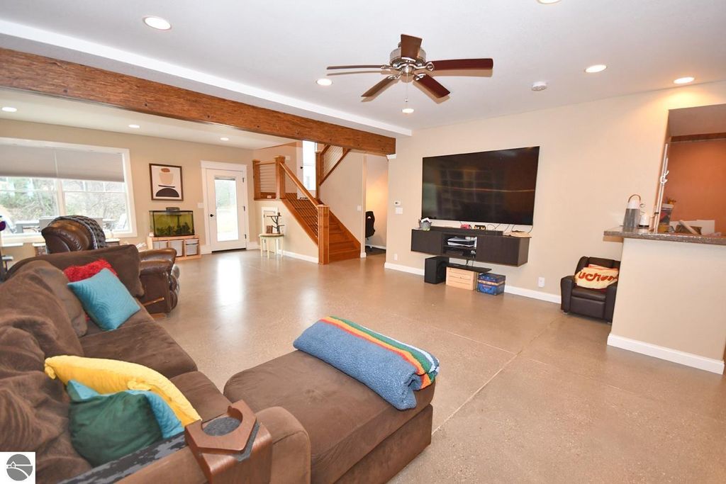 Spacious living room with modern decor, featuring a large sectional sofa, vaulted ceiling with wooden beams, flat-screen TV, and access to a staircase leading to the upper level, showcasing a bright and inviting atmosphere ideal for relaxation and entertainment.