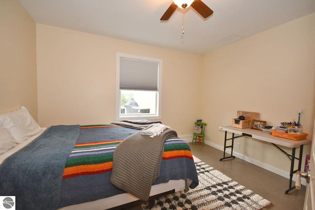 Cozy bedroom featuring a bed with a colorful striped blanket, a window with blinds, and a small desk with office supplies, emphasizing a serene and functional living space in the Maple City property listing.
