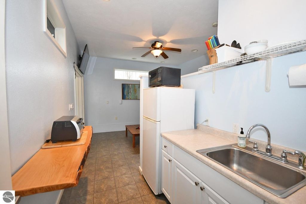 Compact kitchen area featuring a refrigerator, sink, and countertop, with a toaster and microwave, brightened by natural light and a ceiling fan, in a Maple City property listing.