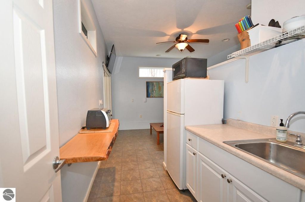 Kitchen area featuring white cabinetry, stainless steel sink, refrigerator, and a small wooden table, with light blue walls and ceiling fan, showcasing a cozy, functional space in a Maple City home.