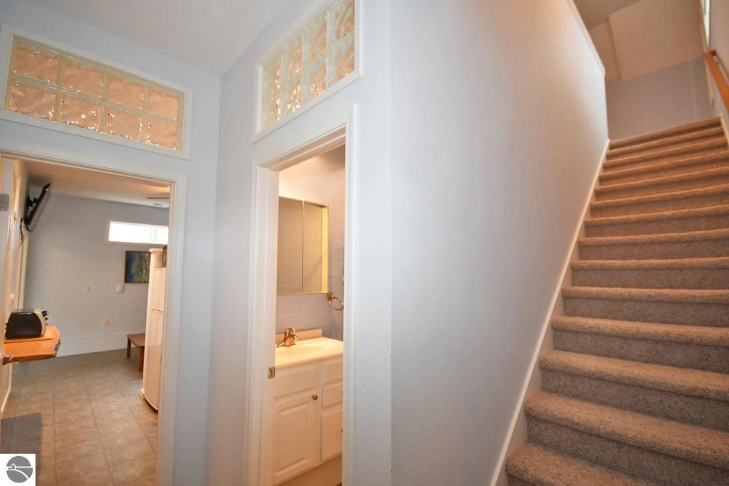 Interior view of a home featuring a staircase, doorway to a bathroom with a sink, and a glimpse of a living area with a table and refrigerator, highlighting the spacious layout and natural light.