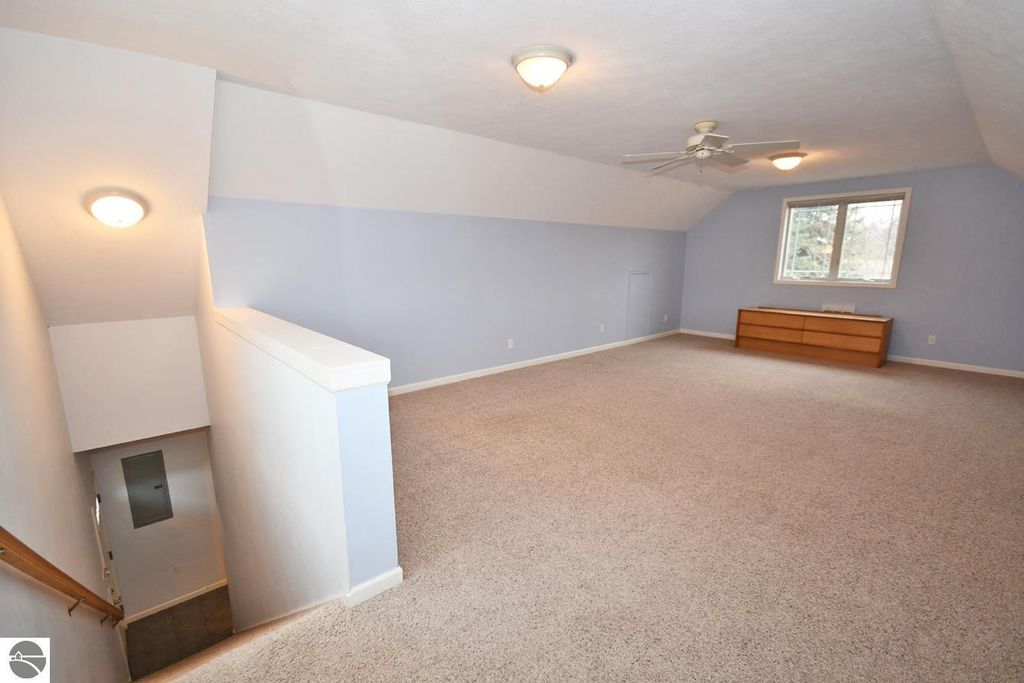 Spacious bonus room above garage with vaulted ceiling, soft carpeting, and large window, showcasing natural light, ideal for office or extra bedroom in Maple City, MI property listing.