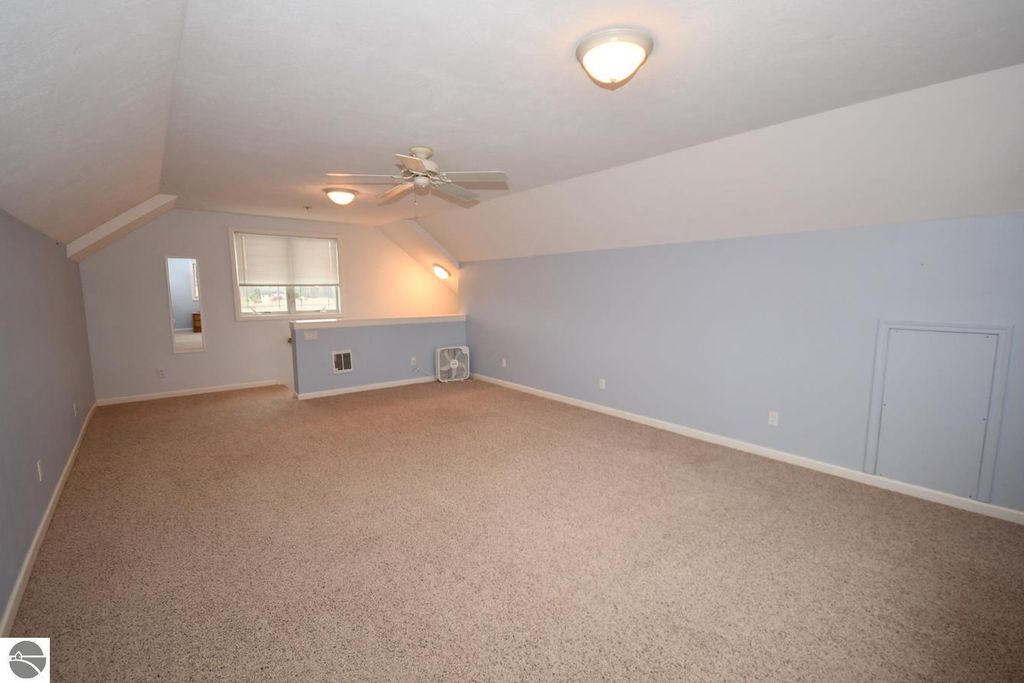 Spacious bonus room with vaulted ceiling, light blue walls, and large windows, featuring carpet flooring and a ceiling fan, ideal for office or additional living space in Maple City home.