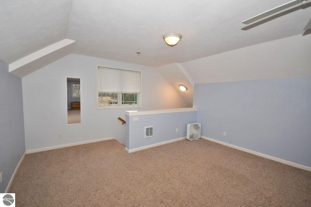 Spacious bonus room with light blue walls, carpet flooring, ceiling fan, and window overlooking the landscape, ideal for office or additional bedroom in Maple City home listing.