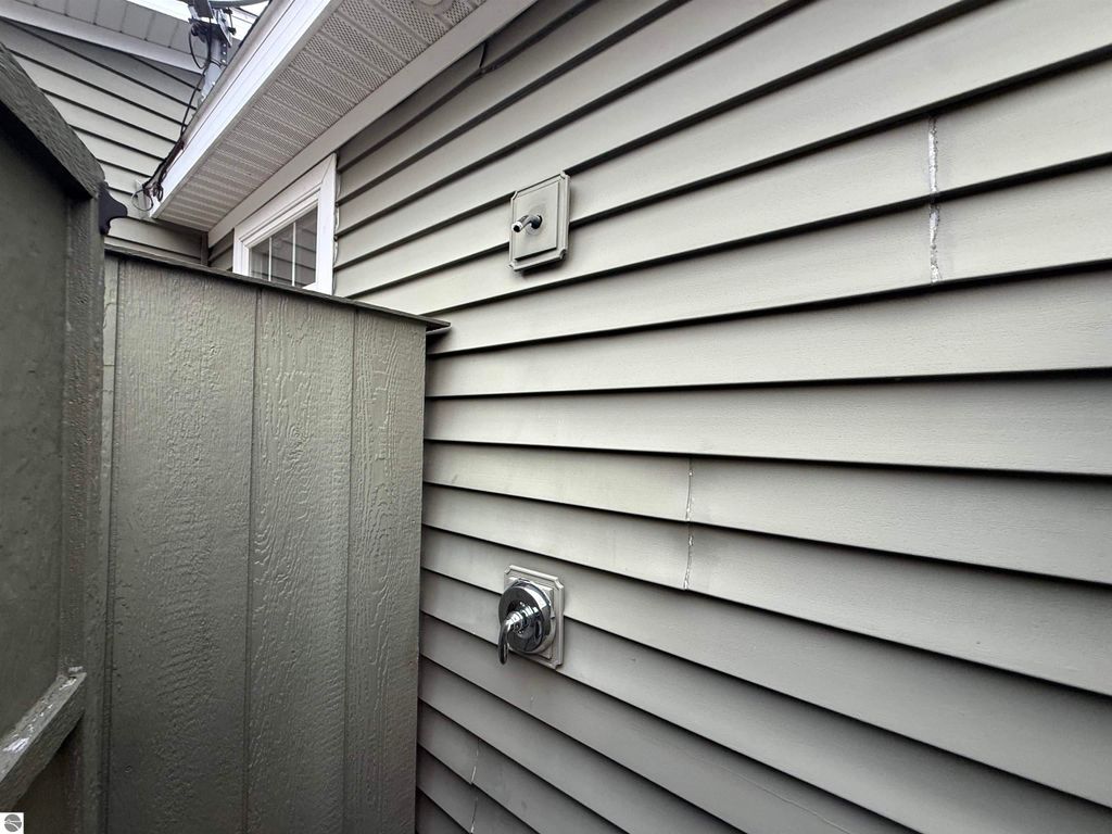 Exterior view of a home's side wall showing utility connections, gray siding, and a wooden privacy fence, relevant to the Maple City property listing at 11007 S Rolling Meadows Drive.
