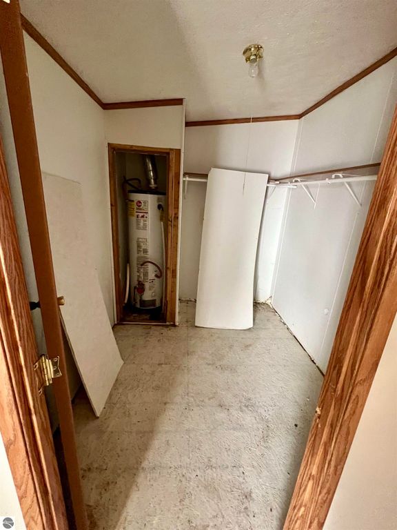 Interior view of a utility room showcasing a water heater, storage space, and unfinished flooring, relevant to the property listing at 9374 Pine Circle Drive NW, Rapid City, MI.