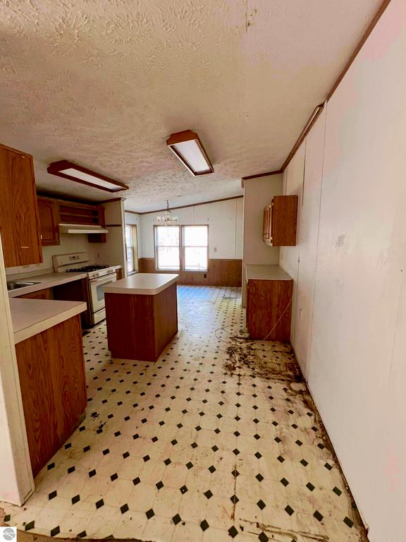 Kitchen interior of a home at 9374 Pine Circle Drive NW, featuring wooden cabinetry, a central island, and visible wear on the flooring, highlighting renovation potential for prospective buyers.