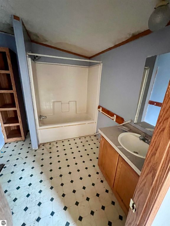 Bathroom interior with a bathtub, sink, and wooden cabinetry, featuring patterned flooring and light blue walls, showcasing potential for updates in the Rapid City home listing.
