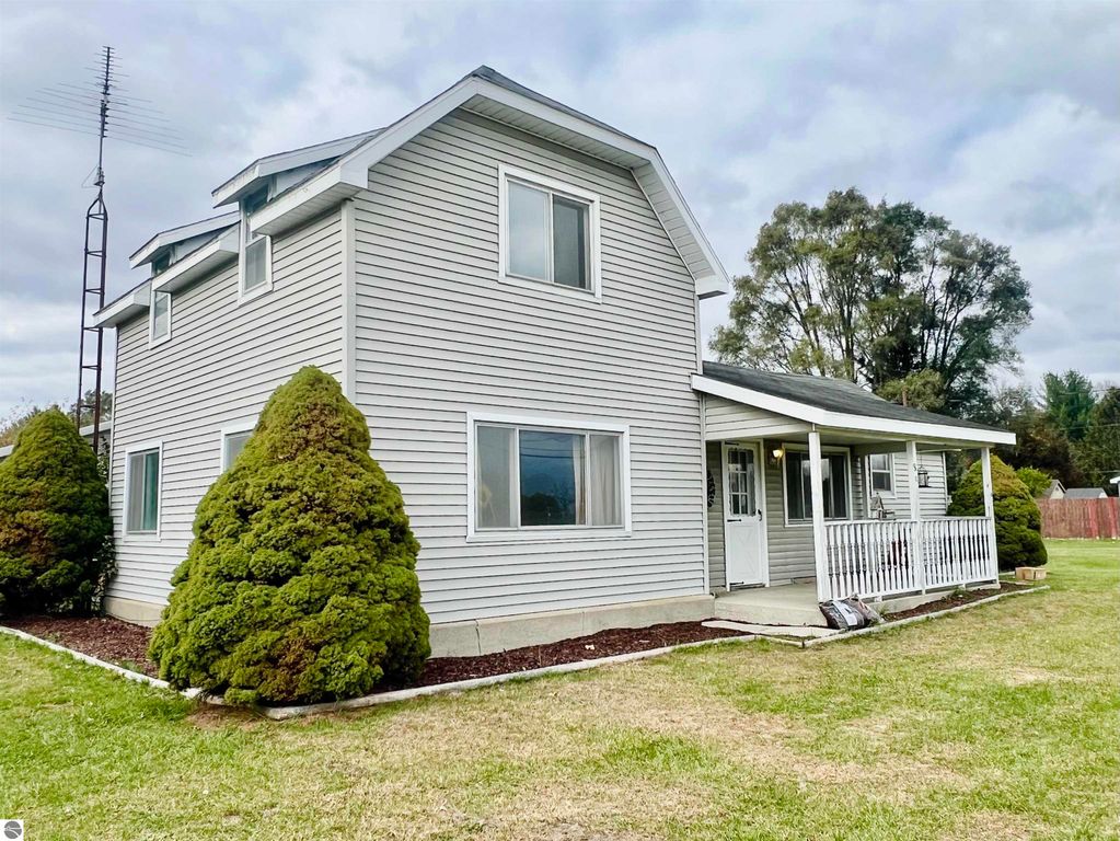 Charming three-bedroom home at 889 N Ferris Road, Sumner, MI, featuring a spacious corner lot, large covered porch, and well-maintained exterior with shrubs.