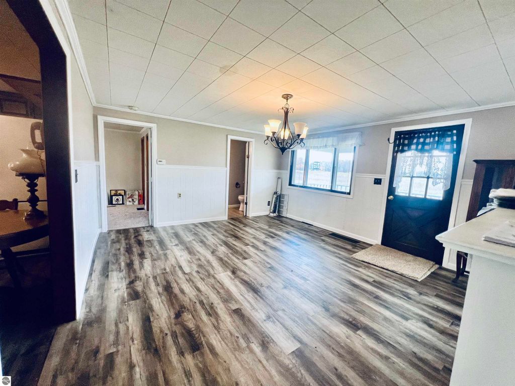 Spacious living room of a charming home at 889 N Ferris Road, featuring wood-like flooring, a chandelier, and large windows, showcasing a welcoming interior perfect for family gatherings.