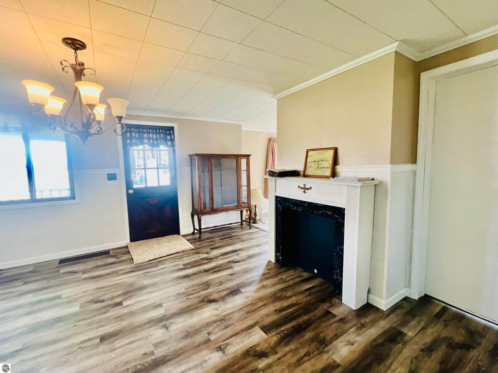Interior view of a charming living room featuring a chandelier, large window, fireplace with black mantel, and a wooden display cabinet, showcasing the warm and inviting atmosphere of the home at 889 N Ferris Road, Sumner, MI.