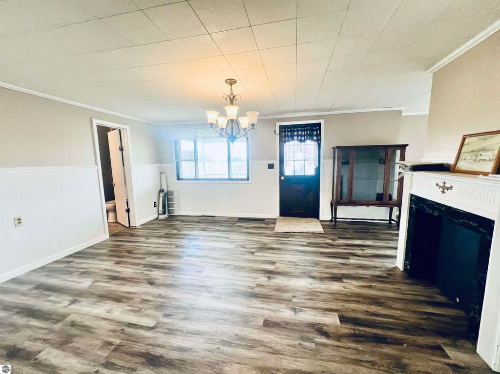 Spacious living room of a three-bedroom home at 889 N Ferris Road, featuring new flooring, a chandelier, and large windows, showcasing a welcoming atmosphere and natural light.