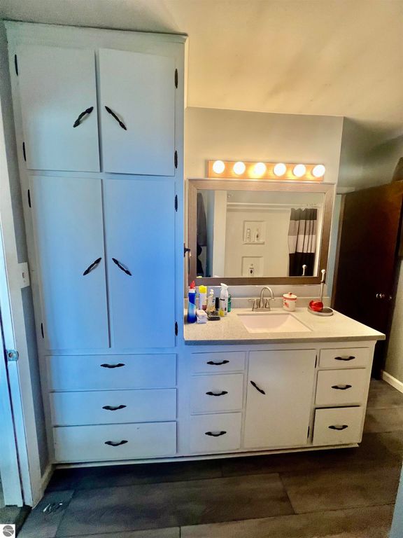 Bathroom vanity with white cabinetry, sink, mirror, and various toiletries, showcasing a clean and functional design in a home at 889 N Ferris Road, Sumner, MI.