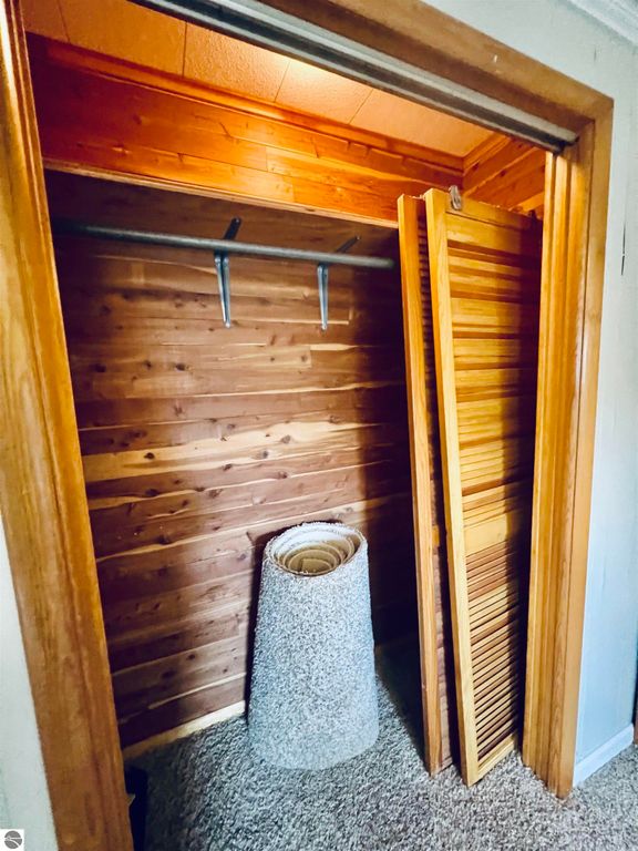 Interior closet with wooden paneling, hanging rod, and a rolled carpet, showcasing a well-maintained space in a three-bedroom home for sale at 889 N Ferris Road, Sumner, MI.