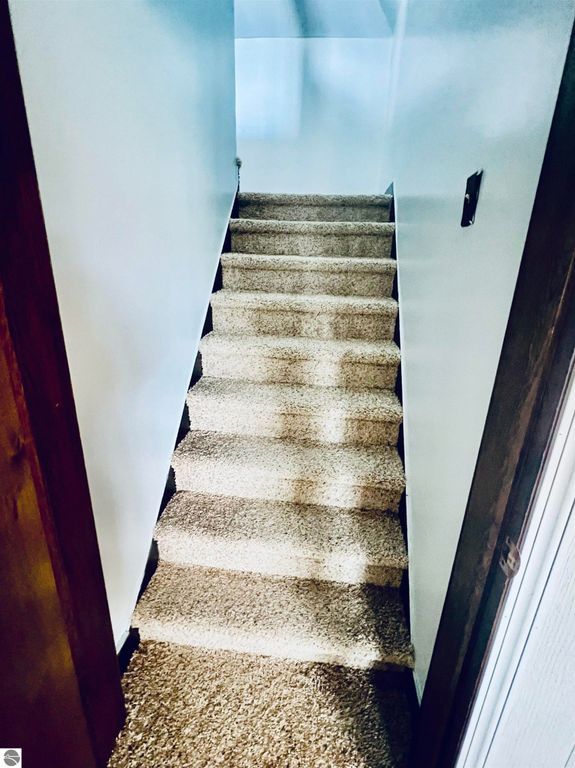 Carpeted staircase leading to the upper level of a three-bedroom home at 889 N Ferris Road, Sumner, MI, highlighting the interior's warmth and inviting atmosphere.