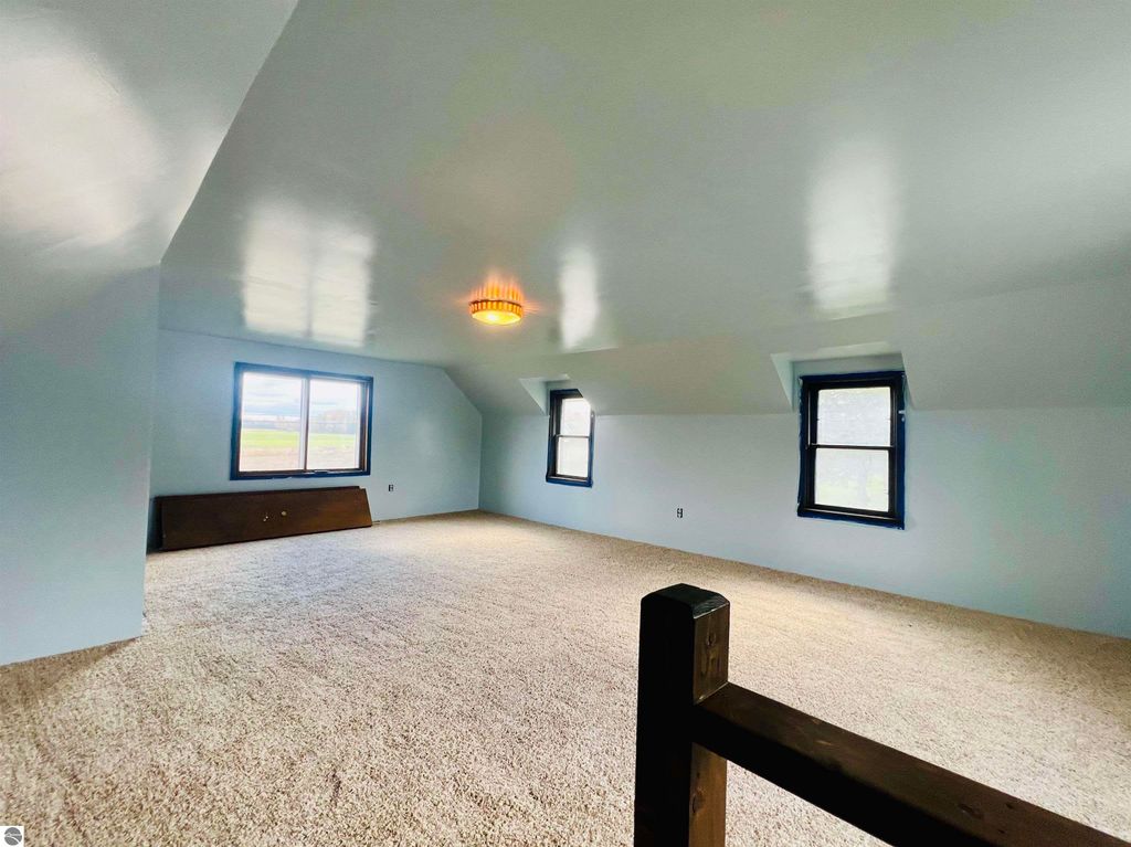 Spacious, carpeted attic room with two windows and a ceiling light fixture, showcasing potential for additional living space in the home at 889 N Ferris Road, Sumner, MI.