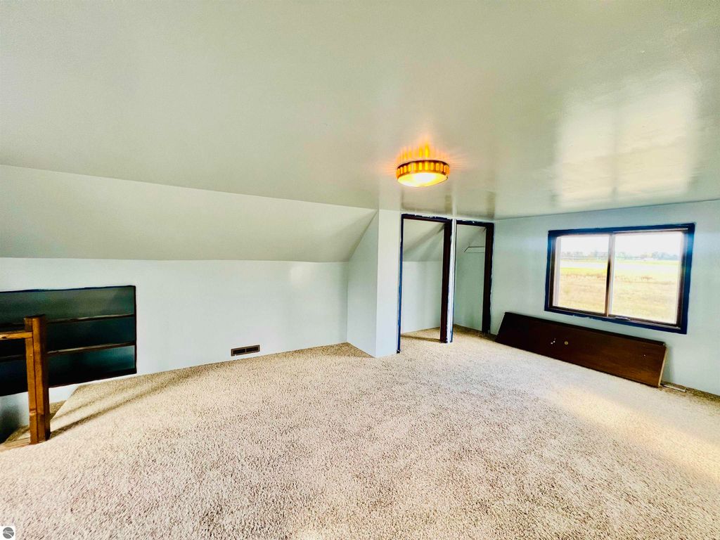 Spacious bedroom with carpeted flooring, sloped ceiling, large window overlooking fields, and closet space, showcasing the charm of the home at 889 N Ferris Road, Sumner, MI.