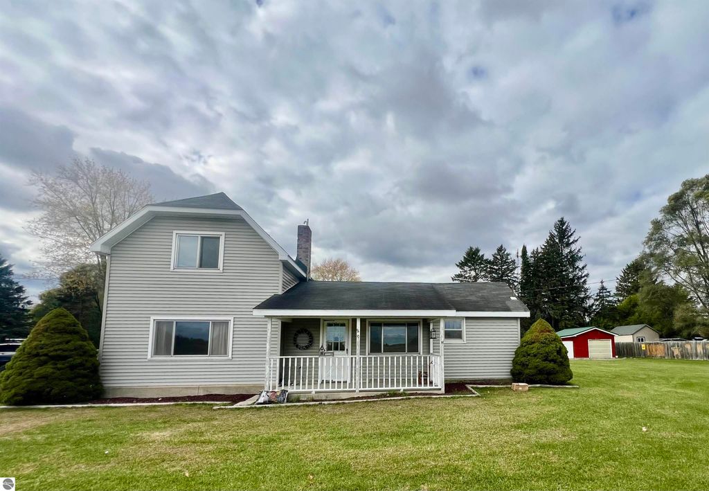 Charming two-story home at 889 N Ferris Road, Sumner, MI, featuring a covered porch, landscaped yard, and surrounding trees, ideal for family gatherings and relaxation.