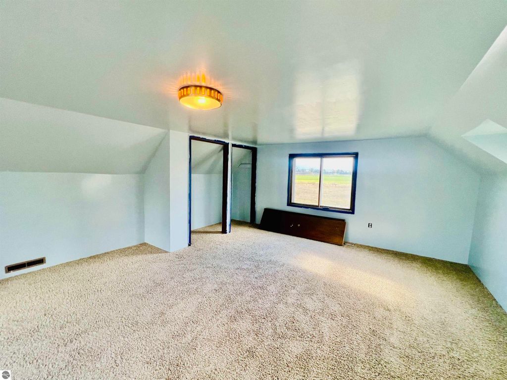Spacious upstairs room with plush carpet, large window offering views, and closet space, featured in the real estate listing for 889 N Ferris Road, Sumner, MI.
