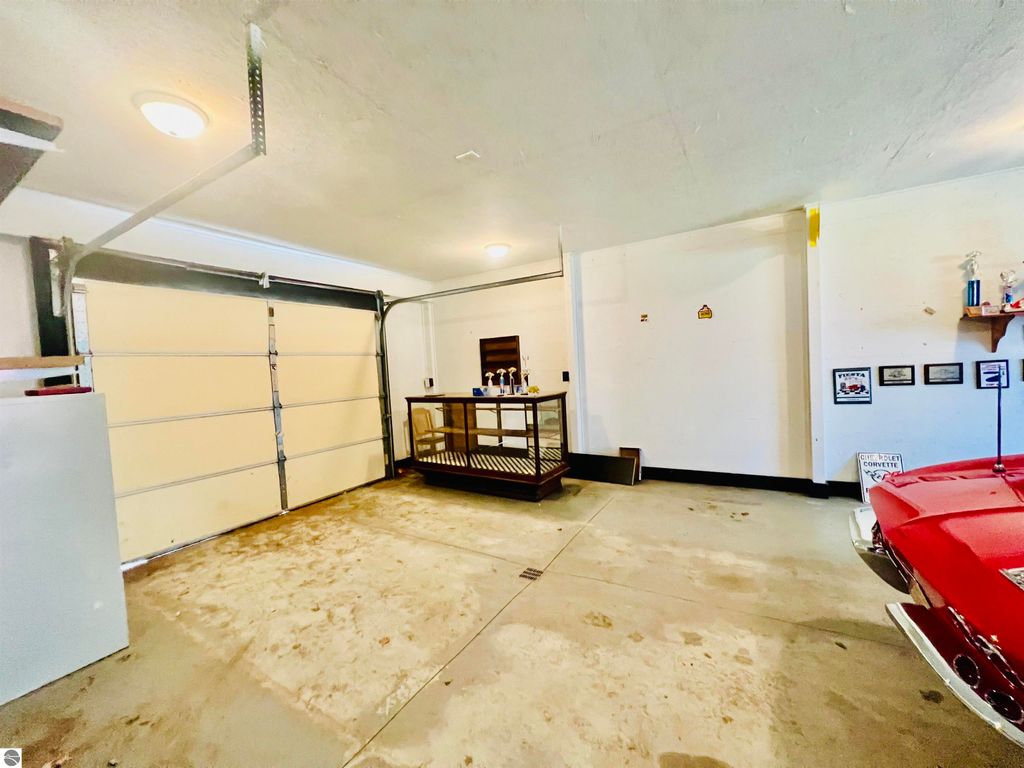Spacious garage interior with concrete floors, featuring a vintage red car, a workbench, and wall-mounted decorations, showcasing ample storage and vehicle space at 889 N Ferris Road, Sumner, MI.