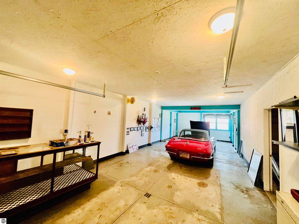 Spacious garage with a classic red car, concrete floors, and storage shelves, showcasing the property's ample space for vehicles and hobbies at 889 N Ferris Road, Sumner, MI.