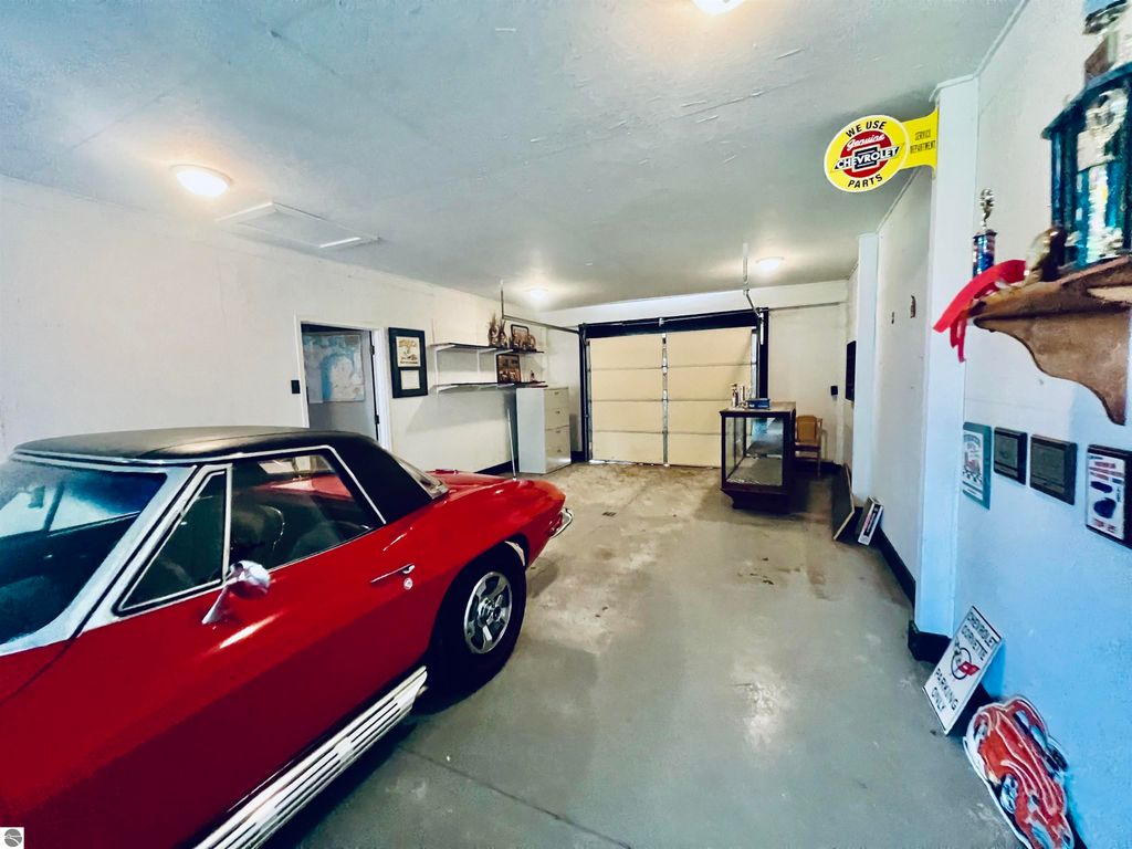 Red vintage car parked in spacious garage with concrete flooring, featuring shelves, a glass display case, and various memorabilia on the walls, highlighting the property's ample garage space at 889 N Ferris Road, Sumner, MI.