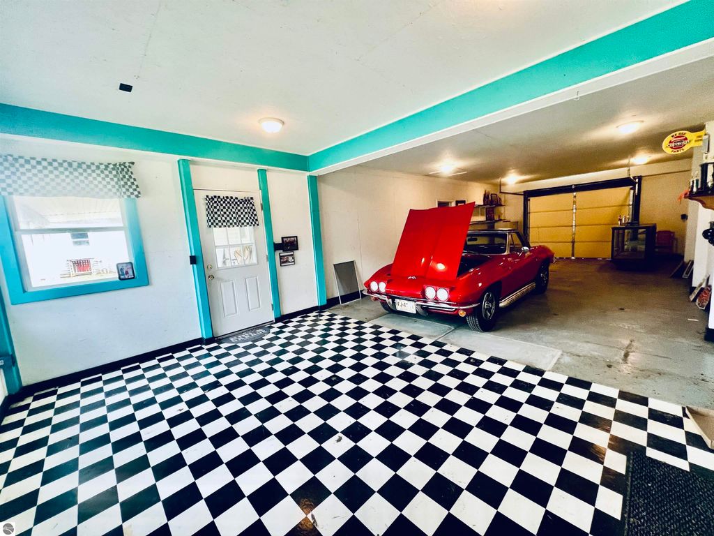 Spacious garage with a classic red car, checkered floor, teal accents, and a door leading outside, showcasing ample space for vehicles and projects at 889 N Ferris Road, Sumner, MI.