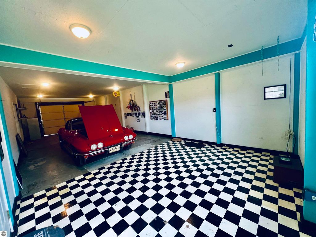 Spacious garage with checkered floor, featuring a classic red car, ample lighting, and wall-mounted photo displays, ideal for vehicle storage and hobbies.