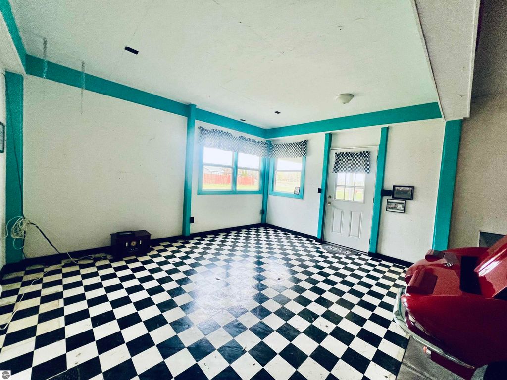 Interior view of a spacious garage with a black and white checkered floor, teal accents on the walls, large windows allowing natural light, and a red car partially visible, reflecting the property's charm at 889 N Ferris Road, Sumner, MI.