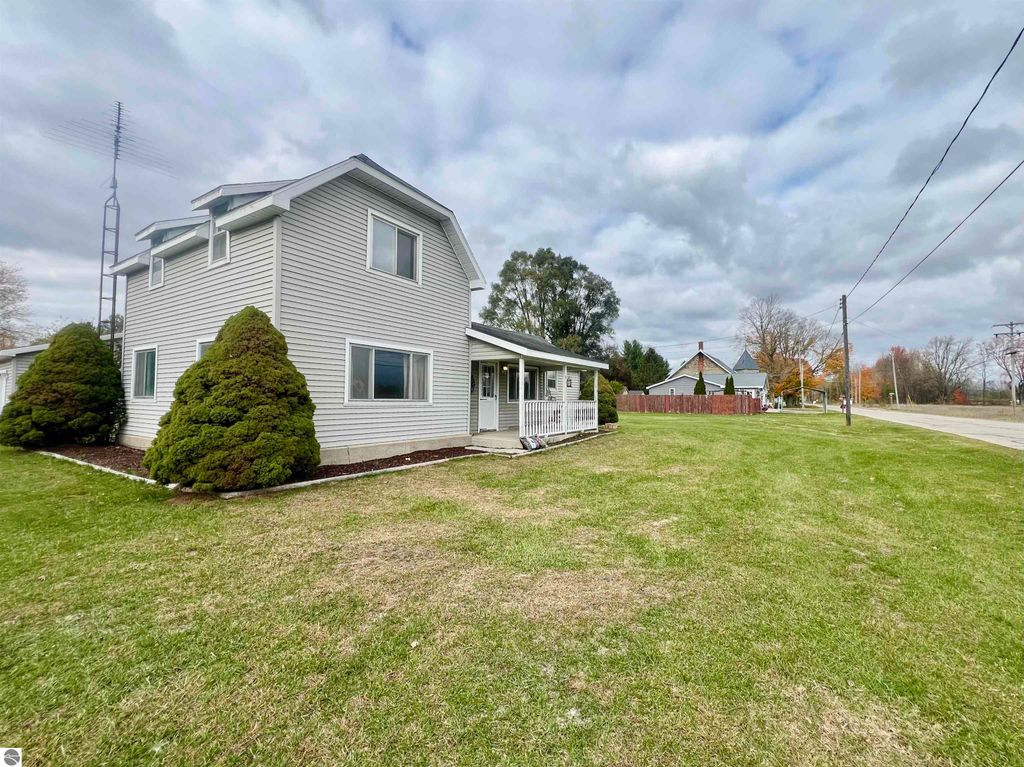 Charming two-story home at 889 N Ferris Road, Sumner, MI, featuring a spacious corner lot, well-maintained landscaping, and a large covered porch, ideal for family gatherings.