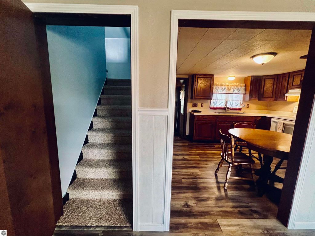 Interior view of a home at 889 N Ferris Road, showing a staircase leading to the upper level and a kitchen area with wooden cabinets and a dining table, emphasizing the cozy and functional layout of the property.