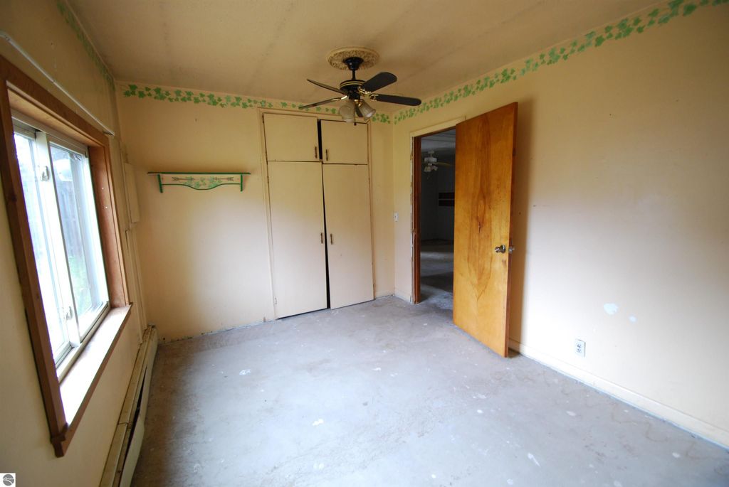 Interior room of a fixer-upper home at 1532 Rabbit Track Drive, Alger, MI, featuring a ceiling fan, unfinished flooring, a window, and closet space, showcasing potential for renovation.