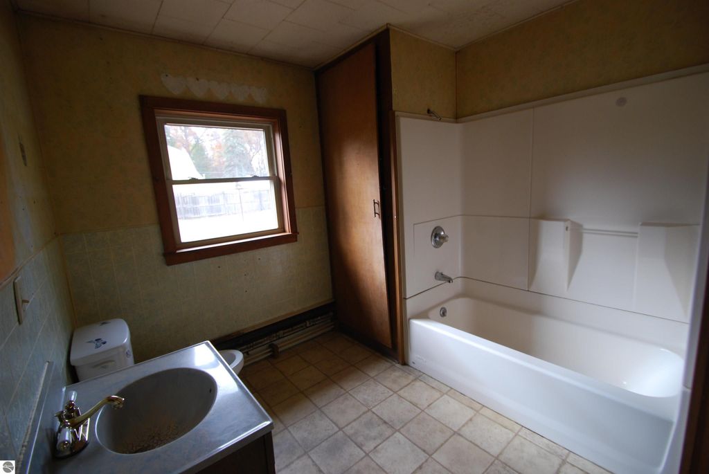 Bathroom interior featuring a bathtub, toilet, and sink, with a window providing natural light, suitable for a fixer-upper home at 1532 Rabbit Track Drive, Alger, MI.
