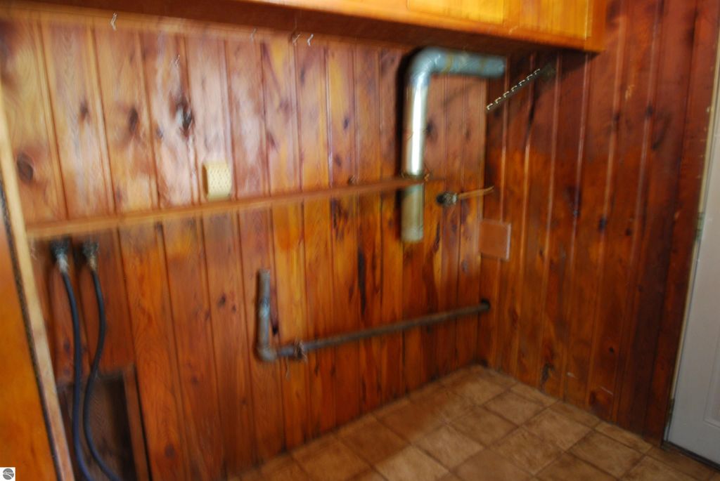 Mudroom interior with wooden paneling, visible plumbing and utility connections, and tiled floor in fixer-upper home at 1532 Rabbit Track Drive, Alger, MI.