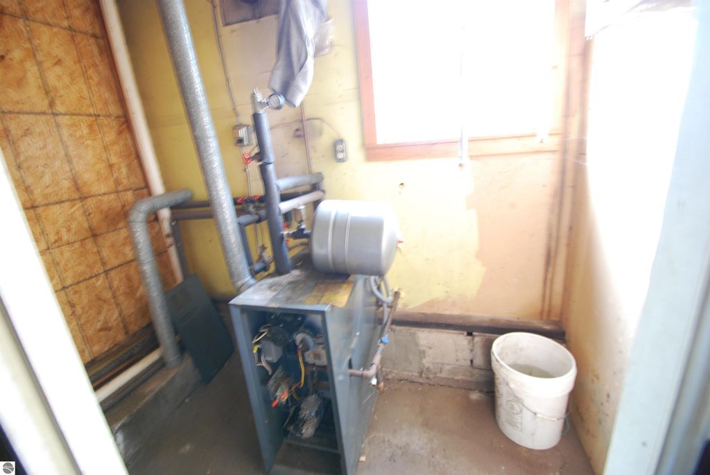 Interior view of a utility room featuring a propane heating unit, exposed pipes, and a white bucket, relevant to the fixer-upper listing at 1532 Rabbit Track Drive, Alger, MI.