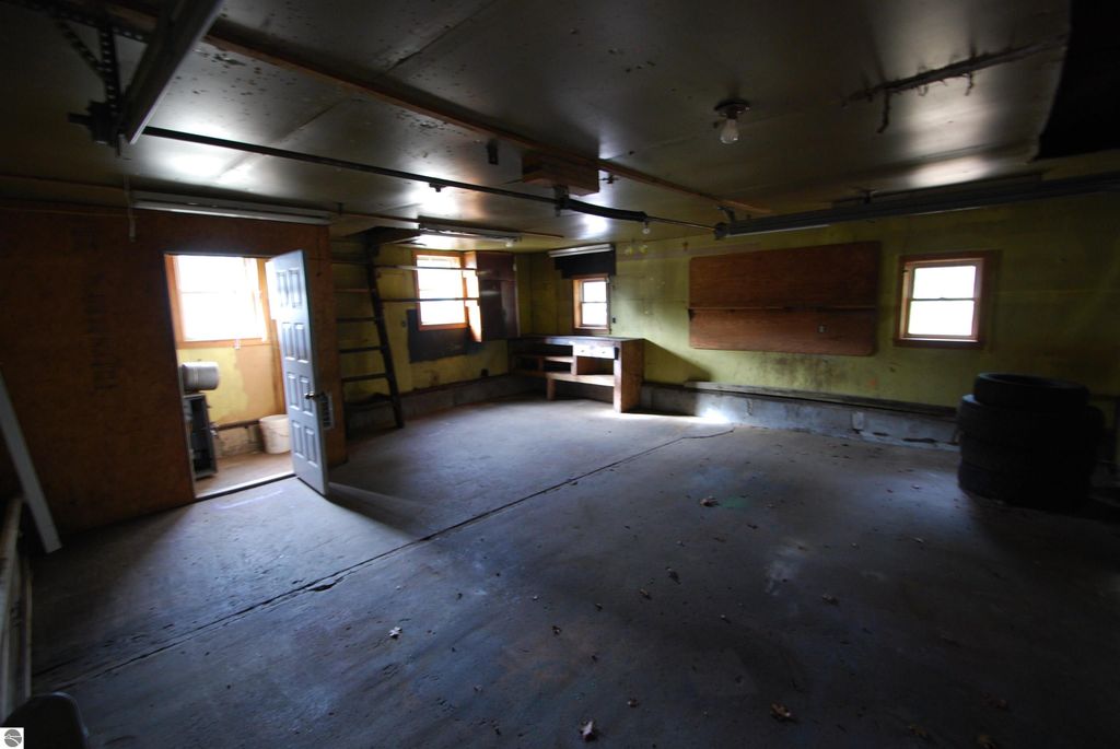 Interior view of a spacious garage with a door leading outside, featuring windows for natural light, a workbench, and tires, highlighting the potential of the property at 1532 Rabbit Track Drive, Alger, MI.