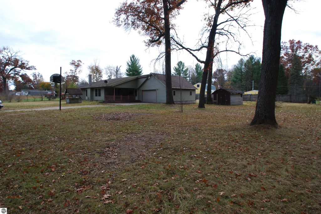 Three-bedroom home at 1532 Rabbit Track Drive, Alger, MI, featuring a spacious yard, attached two-car garage, and garden shed, surrounded by trees and autumn foliage.