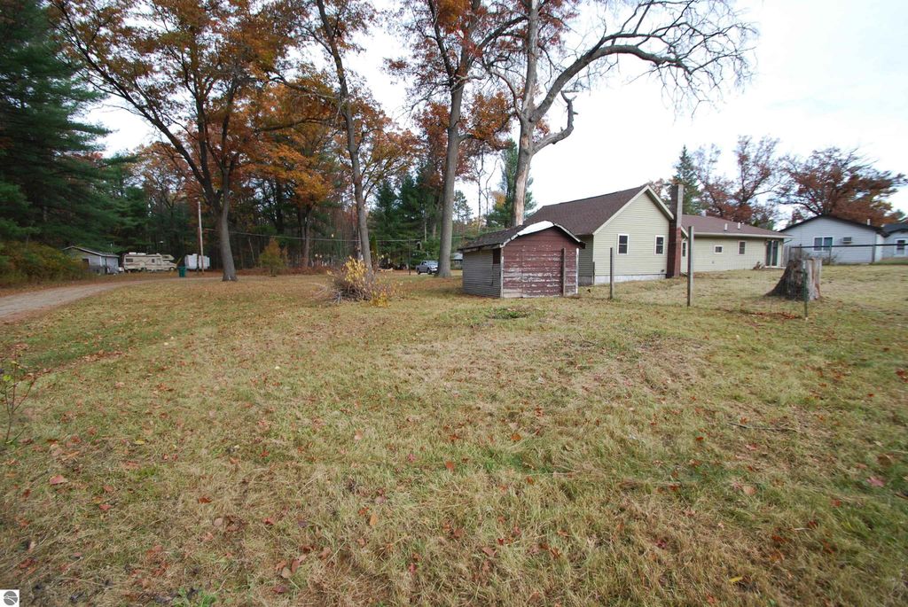 Exterior view of 1532 Rabbit Track Drive, Alger, MI, showcasing a three-bedroom home on a corner lot with an attached garage and garden shed, surrounded by autumn foliage and grassy yard.